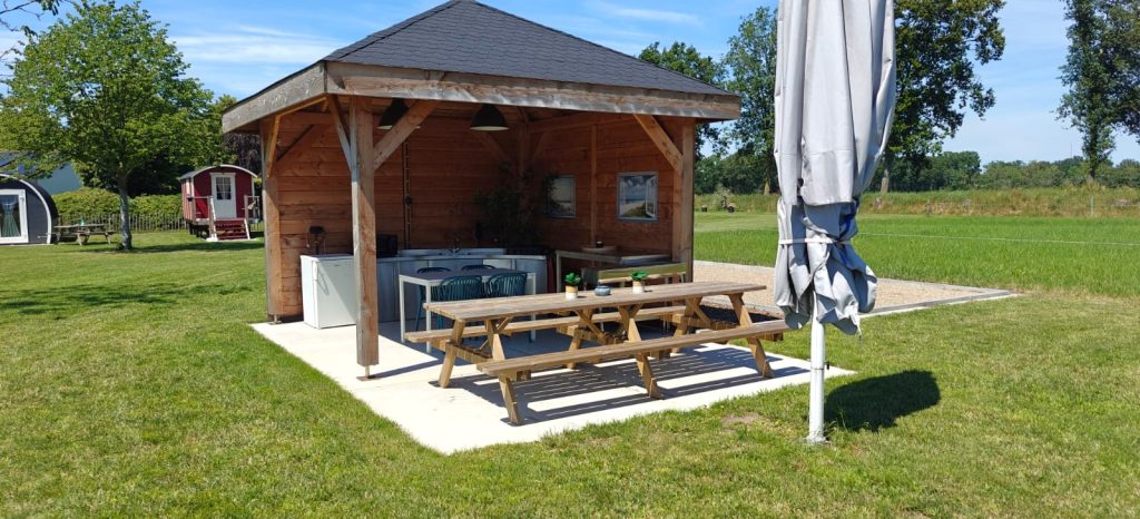 Houten overkapping met lange picknicktafels en buitenkeuken op de camping in Bergeijk