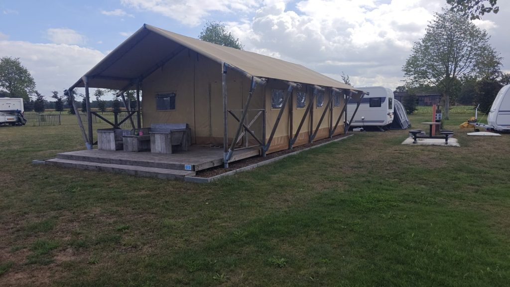 Ruime safaritent met overdekte veranda en picknicktafel, met caravans op de achtergrond