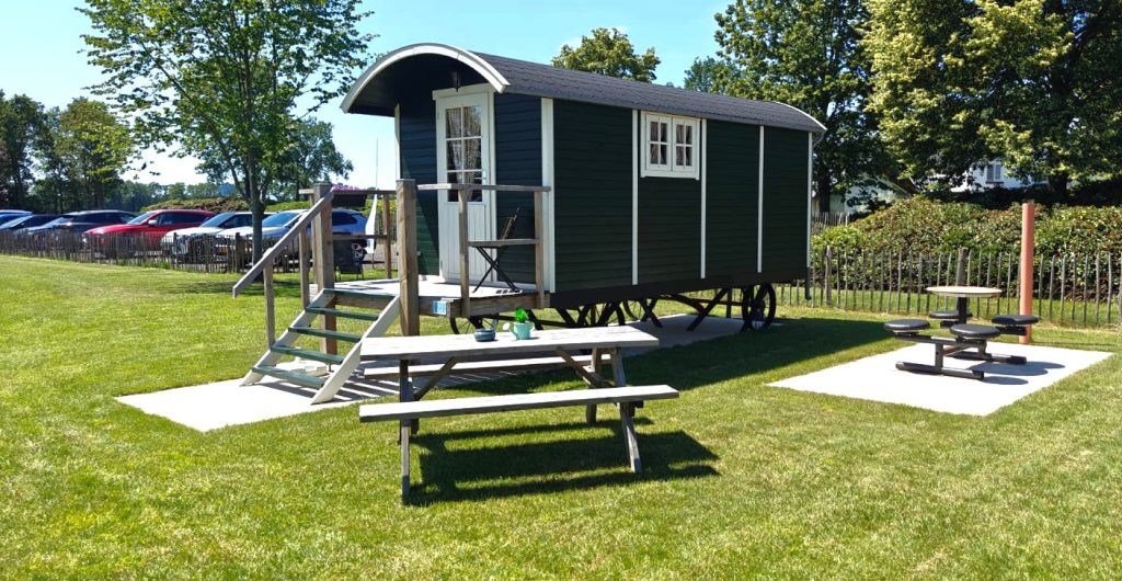 Donkergroene pipowagen met houten terras, trap en picknicktafel op Camping Lindershoeve