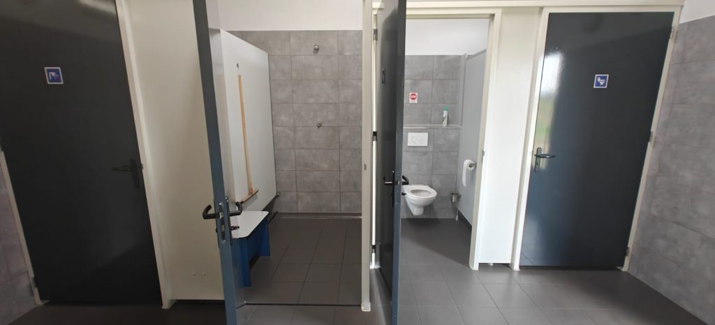 Ruime douchecabine met kleedruimte en een toilet met grijze tegels in het sanitairgebouw van Camping Lindershoeve